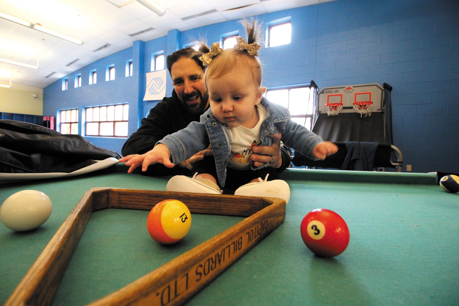 WHERE’S THE EIGHT BALL?: Six-month-old Masie, daughter of Mike and Tiffanie Murdock was introduced to pool by her father as he and his wife worked handing out turkeys and bags of food Saturday at the Boys and Girls Club.